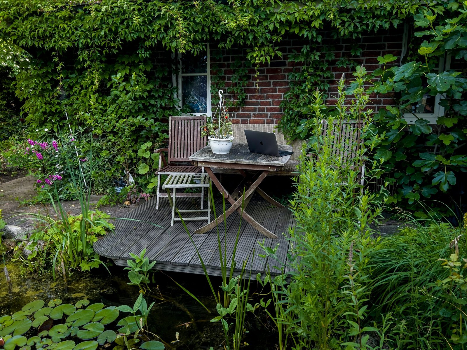 Garden decking with plants surrounding it, furniture includes two wooden chairs and a table.